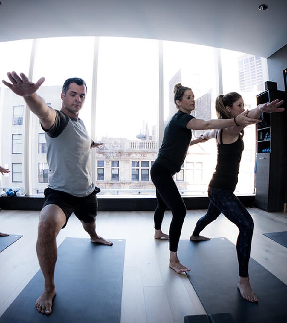 A group yoga class in a fitness studio with floor-to-ceiling windows